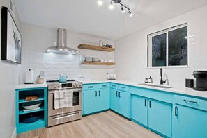 A modern kitchen with teal cabinets, a stainless steel stove, and a window with a view.