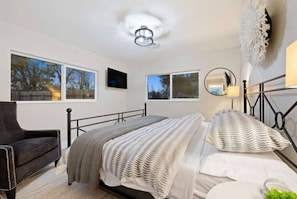 A bedroom with a bed, a chair, and two windows.