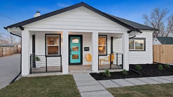 A single-story house with a front porch, a turquoise door, and a small garden area.