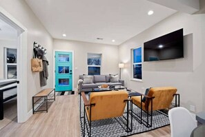 A modern living room with a sofa, coffee table, and chairs, a teal door, and a TV mounted on the wall. - SuperChic Farmhouse*Old Town Arvada*LightRail*Dogs (Arvada)
