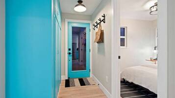 A hallway with a teal door leading to a bedroom with a bed and a nightstand.