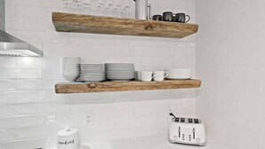 A kitchen with white tiled backsplash, wooden shelves holding plates, cups, and a kettle, and a white toaster on the counter. - SuperChic Farmhouse*Old Town Arvada*LightRail*Dogs (Arvada)