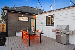 A patio with a wooden deck, a table with orange chairs, a grill, and string lights.
