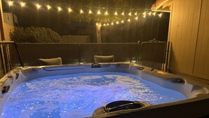 A hot tub with a blue light, surrounded by a fence and string lights.