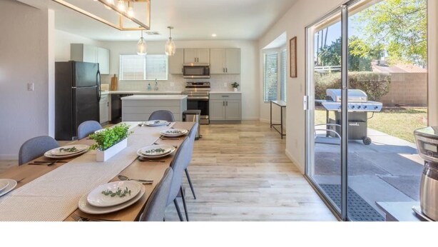 A modern kitchen with a dining area, large windows, and a barbecue grill outside.