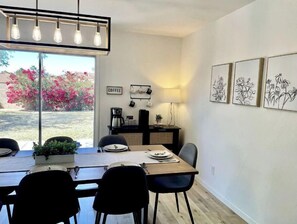 Un comedor con una mesa preparada para cuatro personas, una estación de café e impresiones enmarcadas de motivos botánicos en la pared.