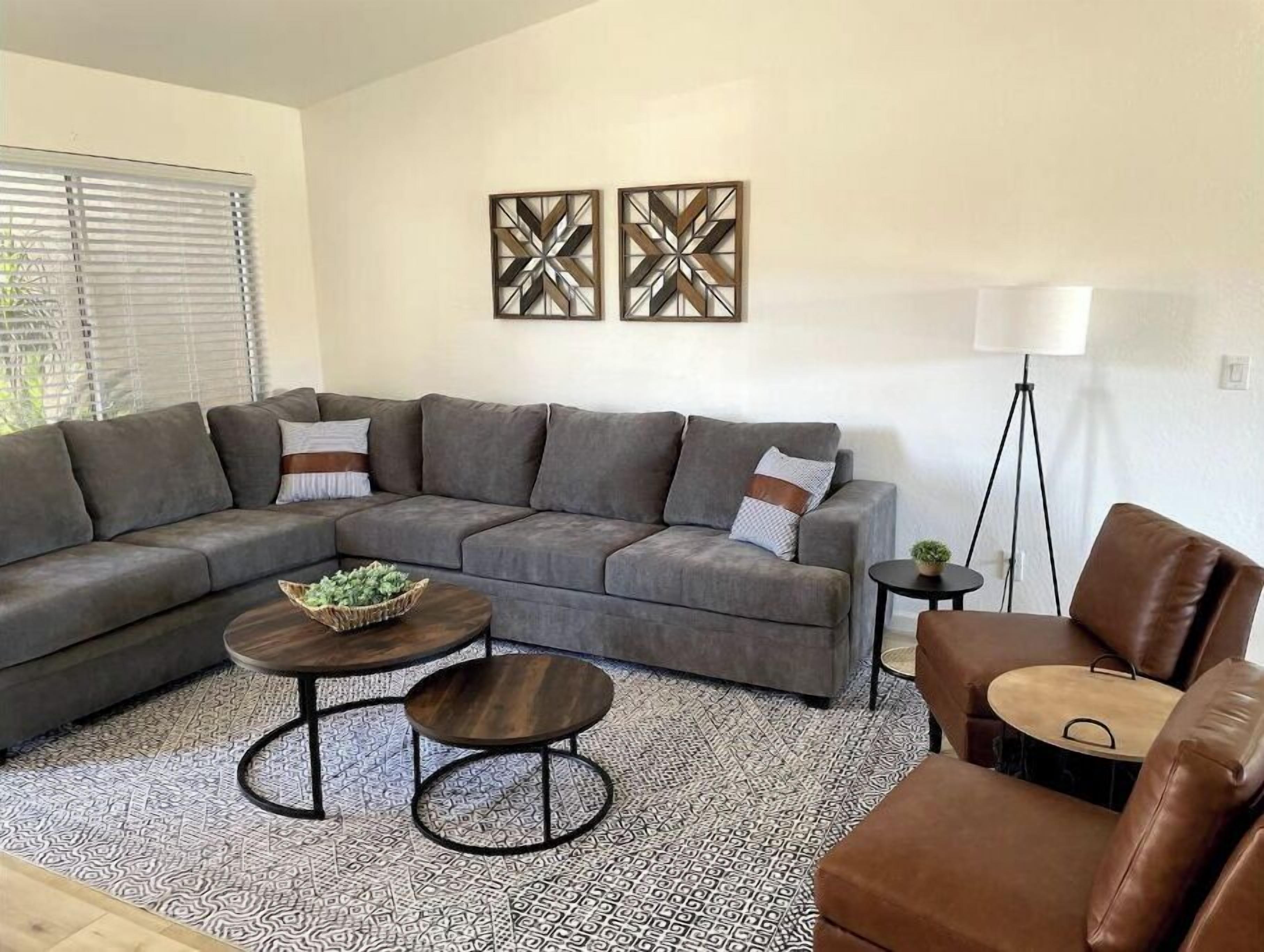 A living room with a grey sectional sofa, two round coffee tables, a brown leather armchair, and a floor lamp.