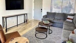 A modern living room with a grey sofa, a TV mounted on the wall, a console table, and a patterned rug.