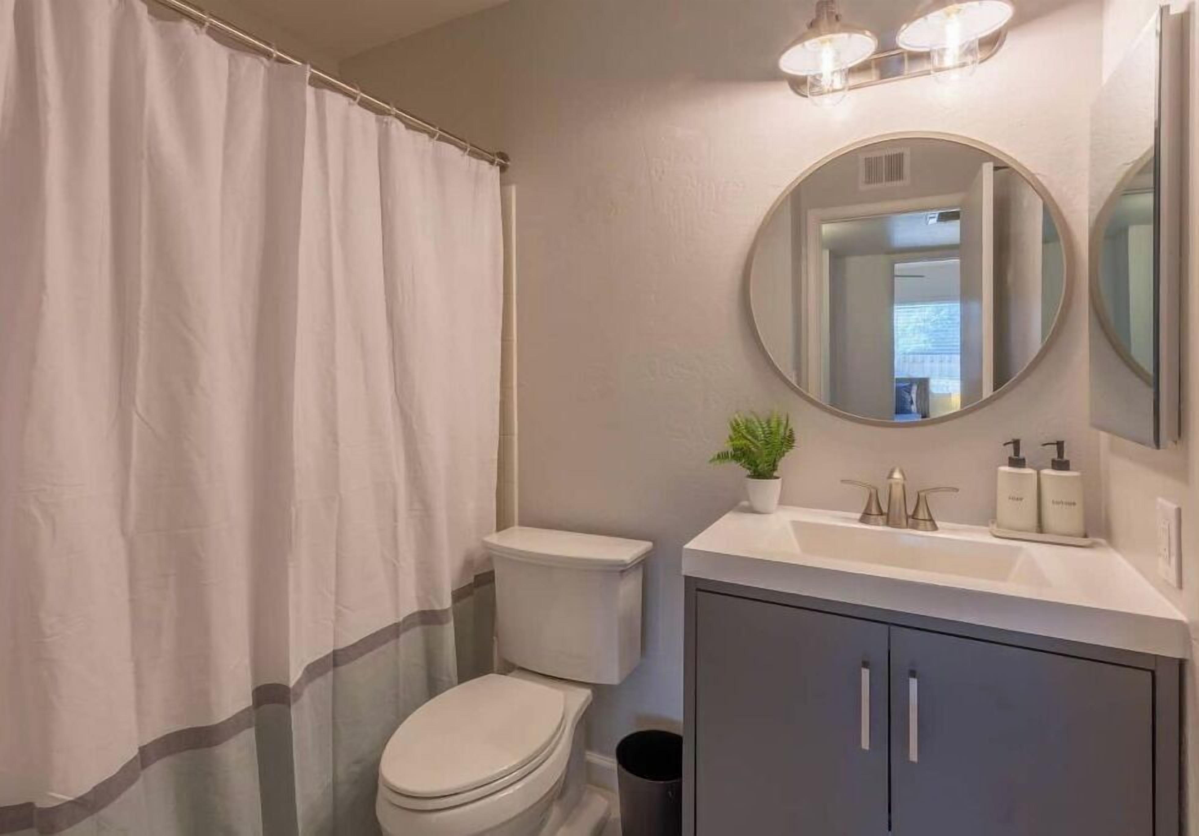 Un baño con inodoro, lavamanos y espejo, y una cortina de ducha.