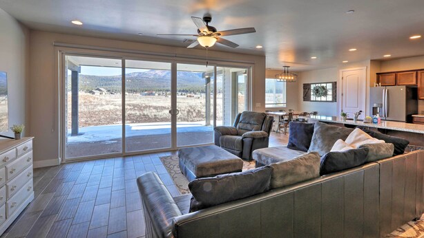A spacious living room with a large sofa, a ceiling fan, and a view through a sliding glass door to the outdoors. - Flagstaff Home w/ Views - Near Arizona Snowbowl! (Flagstaff)