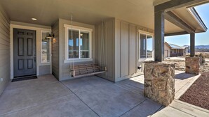 A covered porch with a bench, a stone planter, and a door with a window. - Flagstaff Home w/ Views - Near Arizona Snowbowl! (Flagstaff)