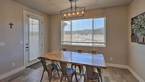 A dining area with a wooden table and metal chairs, a chandelier, a window with blinds, and a door with a doormat. - Flagstaff Home w/ Views - Near Arizona Snowbowl! (Flagstaff)