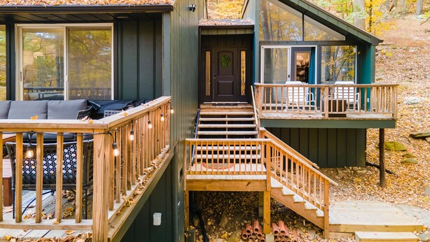 A cabin with a deck, a staircase, and a large window overlooking a forest. - Private hot tub, wooded, EV charger, 1-gig fiber internet (Berkeley Springs)