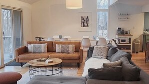 A spacious living area with a high ceiling, a dining table, and a kitchen area visible through an open door. - Private hot tub, wooded, EV charger, 1-gig fiber internet (Berkeley Springs)