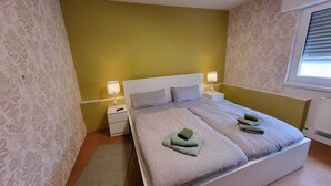 A bedroom with a large bed, two bedside tables, and a window with blinds. - Large bright vacation apartment_only for private guests_ no fitters (St. Leon-Rot)