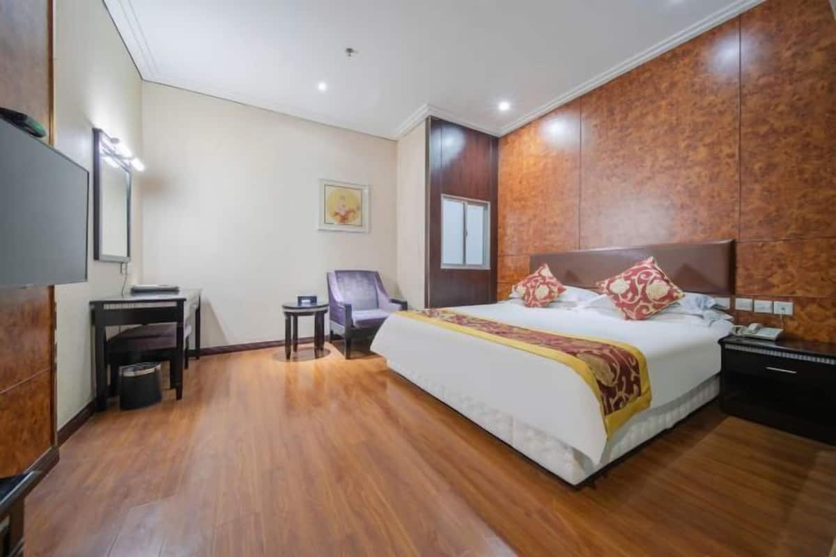 A hotel room with a bed, a desk, a chair, a TV, and a small table.