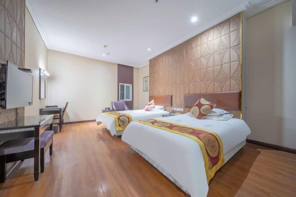 A hotel room with two beds, a desk, and a television.