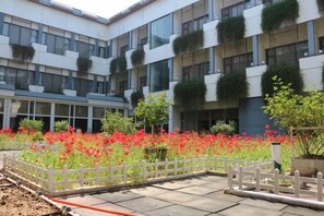 Une cour avec une clôture blanche, des fleurs rouges et un immeuble à plusieurs étages doté de balcons.