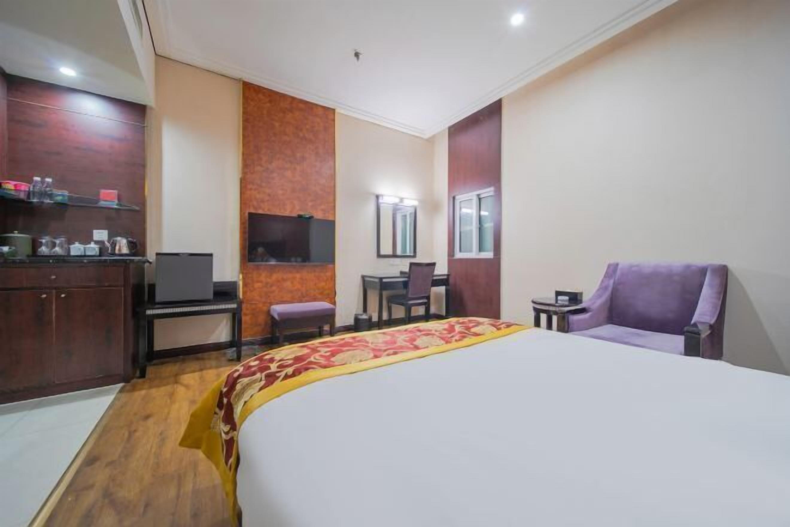 A hotel room with a bed, a desk, a chair, a TV, and a small table.