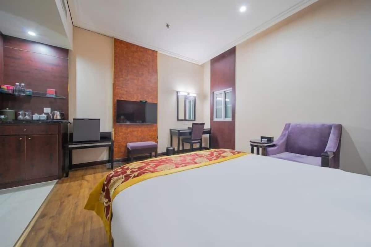 A hotel room with a bed, a desk, a chair, a TV, and a small table.
