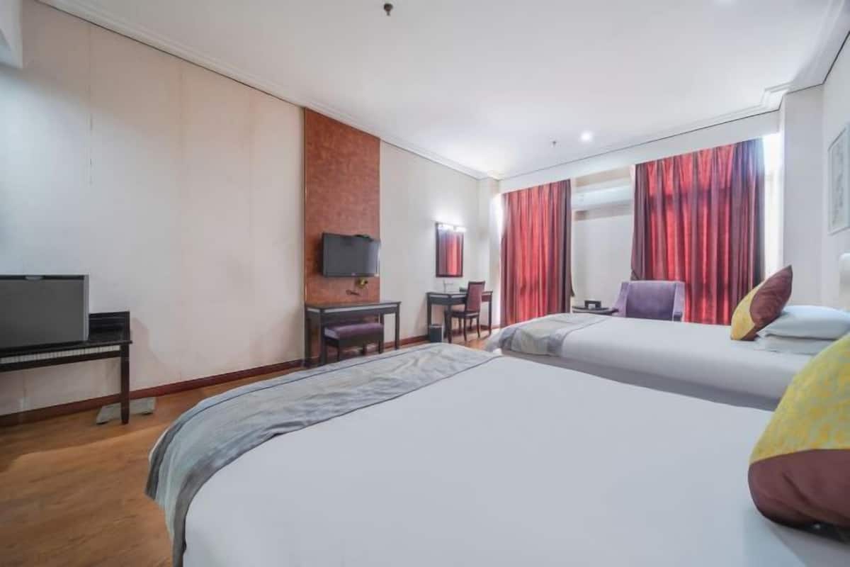 A hotel room with two beds, a desk, a chair, a television, and a window with red curtains.