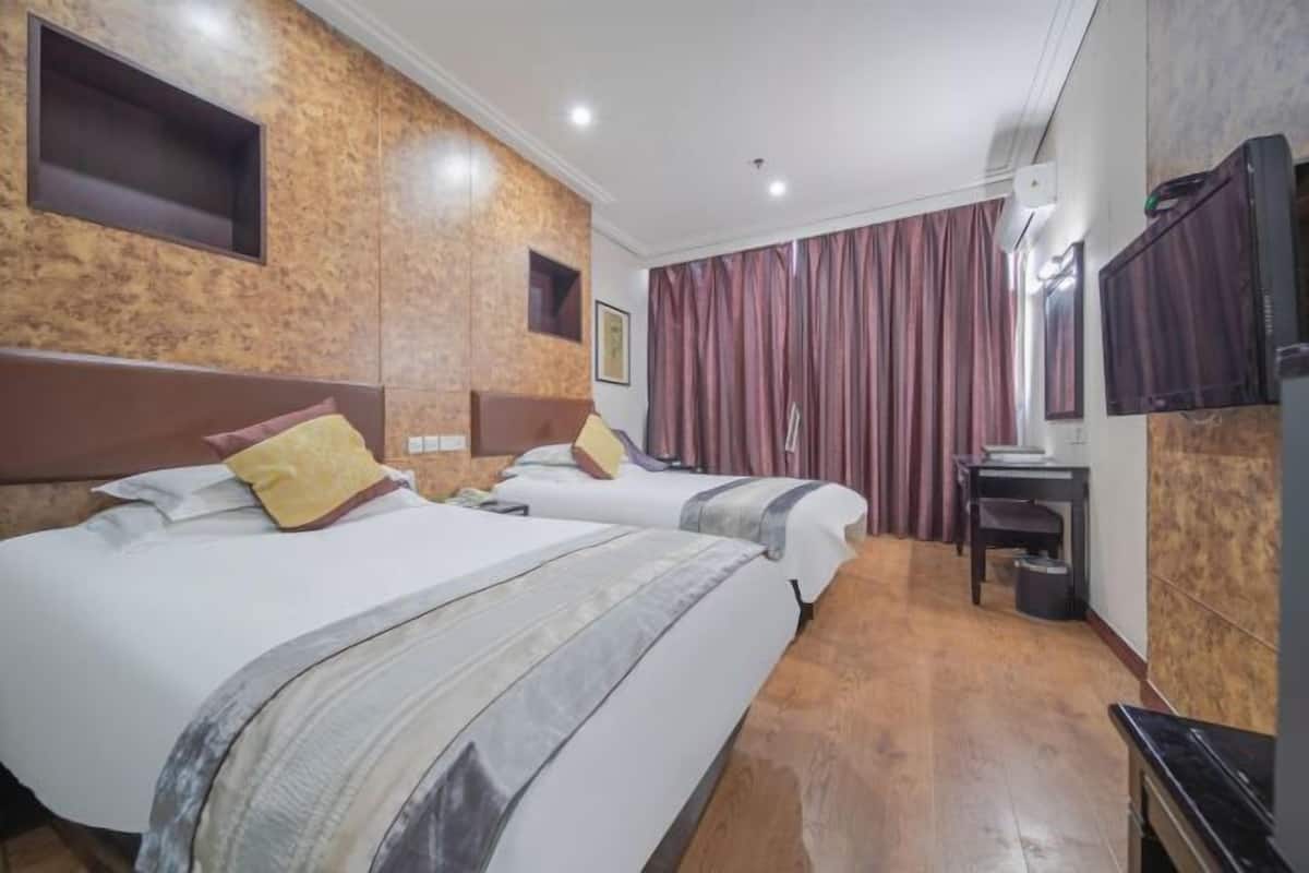 A hotel room with two beds, a desk, a chair, a television, and a large window with curtains.