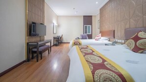 A hotel room with two beds, a desk with a chair, a television, and a window.