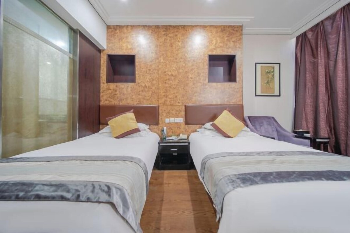 A hotel room with two beds, a wooden accent wall, a nightstand, and a framed picture on the wall.