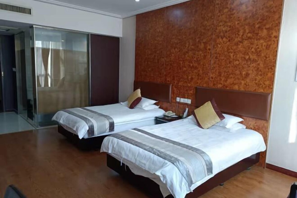 A hotel room with two beds, a wooden floor, a glass door, and a textured wall.