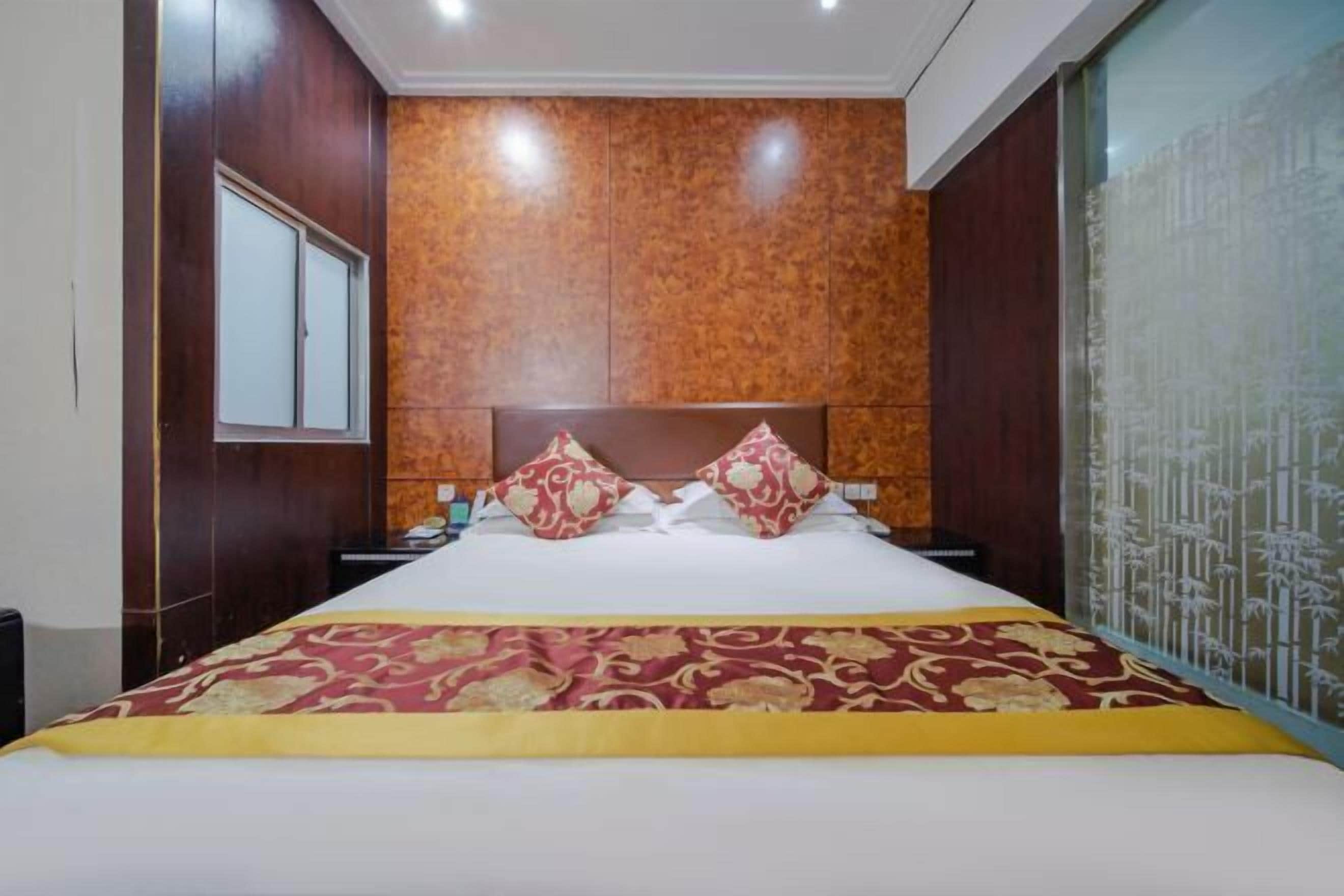 A hotel room with a large bed, a wooden headboard, a window, and a decorative wall panel.