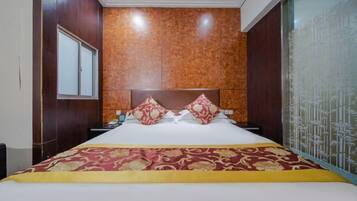 A hotel room with a large bed, a wooden headboard, a window, and a decorative wall panel.