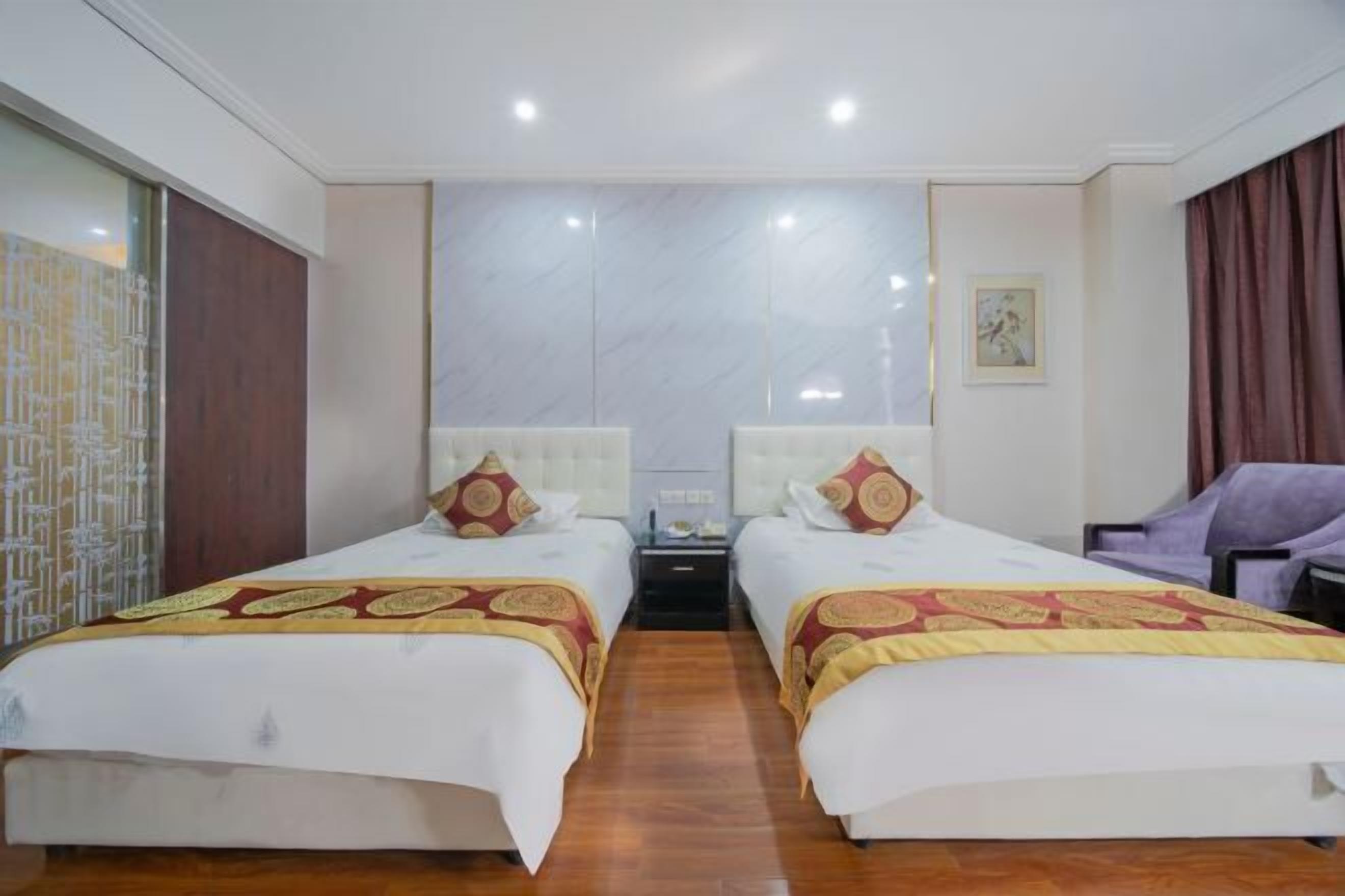 A hotel room with two beds, a nightstand, a chair, and a large mirror.