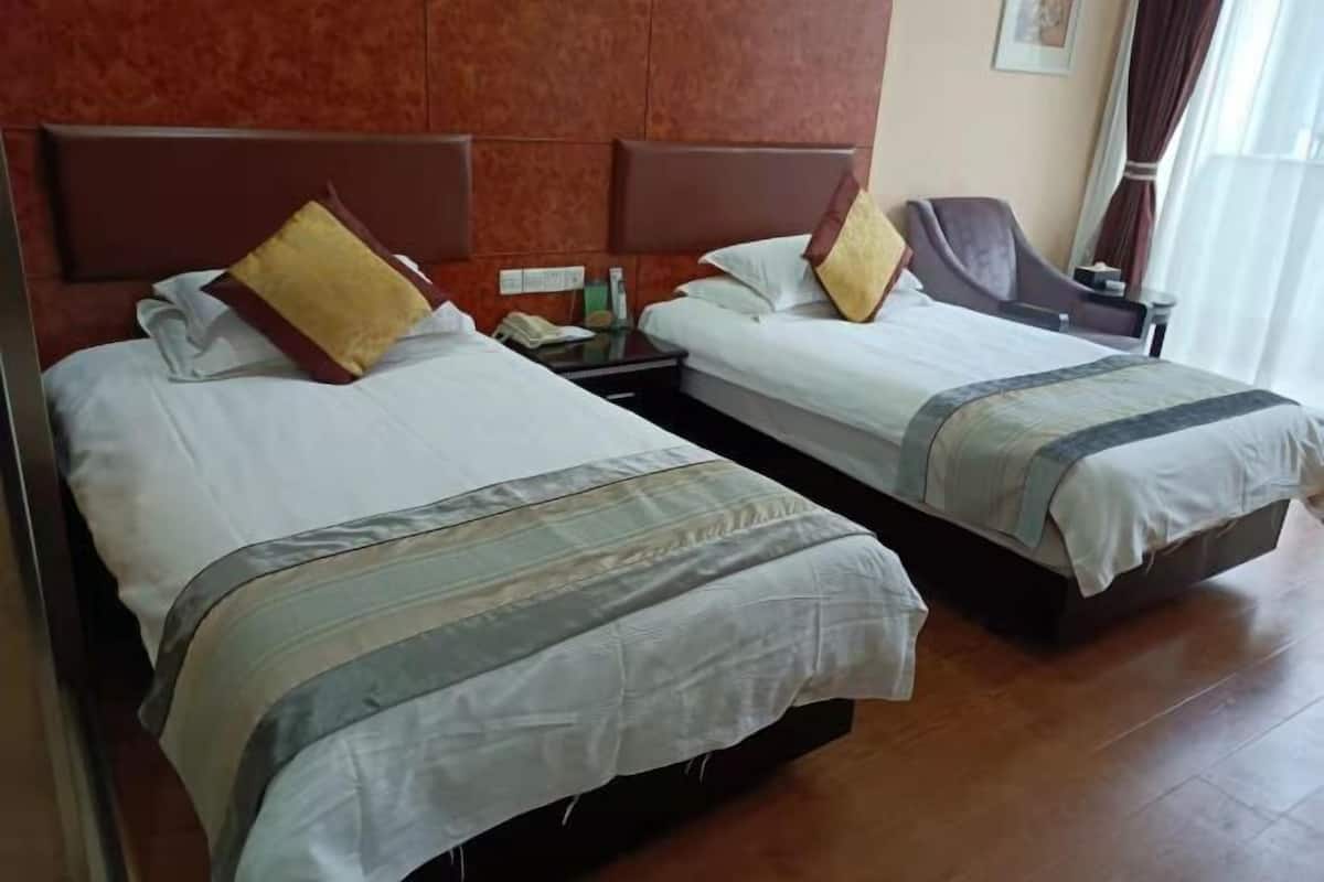 Two beds with headboards, a bedside table with a phone, and a window with curtains.