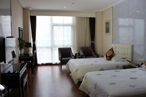 A hotel room with two beds, a desk with a computer, a chair, and a large window with curtains.