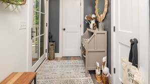 Un couloir avec un tapis à motifs, un banc en bois, une porte et un miroir au mur.