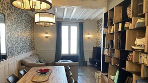 A cozy living room with a wooden dining table, a sofa, and a bookshelf filled with books and decorative items. - Villa quai du Treport 4* facing port and sea. (Le treport)