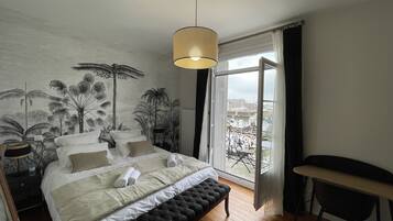 Een slaapkamer met een groot bed, een bankje, een bureau en uitzicht op de stad door een groot raam.