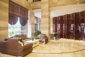 Eine geräumige Lobby mit hoher Decke, einer Sitzecke mit Sofas und Sesseln sowie einem großen Fenster mit Vorhängen.