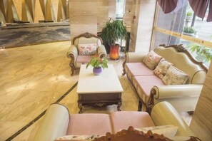 A lobby with a marble floor, a white coffee table with a plant, and a sofa with floral cushions.