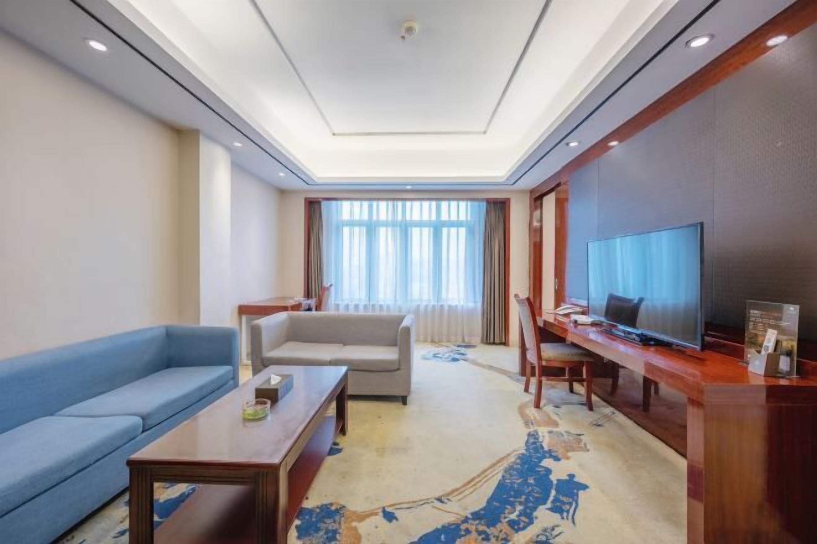 A modern hotel room with a sofa, a coffee table, a TV, and a desk.