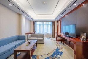 A modern hotel room with a sofa, a coffee table, a TV, and a desk.