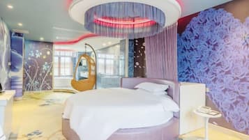 A modern hotel room with a circular bed, a hanging chair, and a large floral wall mural.