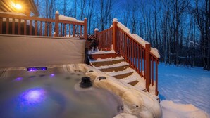 Un escalier en bois menant à un espace équipé d’un bain à remous, avec de la neige sur les marches et les rampes.