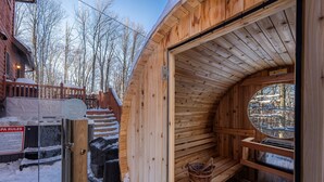 Un sauna en bois offrant une vue sur un paysage enneigé, avec une terrasse en bois à l’extérieur.