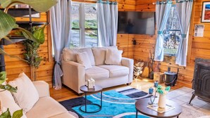 Une pièce confortable, aménagée comme un chalet, avec un canapé beige, une petite table ronde et un tapis bleu à motifs.