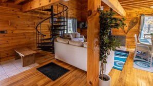 L’intérieur d’un chalet en bois, avec un escalier en colimaçon, un canapé, une table à manger et une plante en pot.