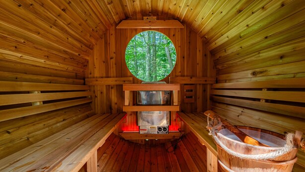 Un sauna avec des murs en bois, une fenêtre circulaire, un banc et une baignoire en bois.