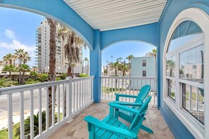 A balcony with turquoise chairs, white railings, and a view of palm trees and buildings. - Directly Across from Beach! Dog-Friendly Home with Private Pool! (South Padre Island)