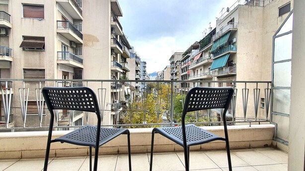 Un balcon avec deux chaises, donnant sur un quartier résidentiel composé de plusieurs immeubles.