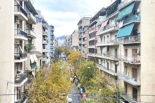 A narrow street flanked by multi-story residential buildings with balconies, a clear sky, and autumn foliage. - Vacation Home For 4 - ENTIRE FLAT (Athina)